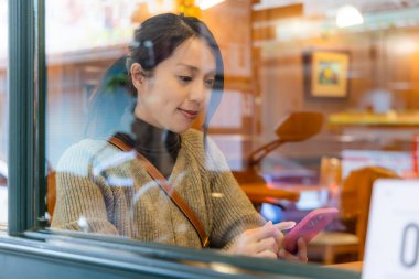 Kadın cep telefonu kullanıyor ve pencere yansıması ile kafenin içinde oturuyor