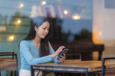 Kadınlar cep telefonu kullanır ve kahve dükkanında otururlar.