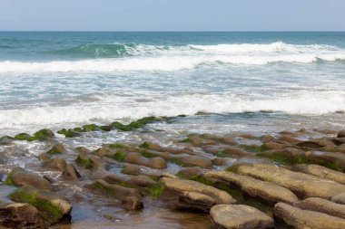 Deniz dalgası kayalıkların üzerine sıçrıyor.