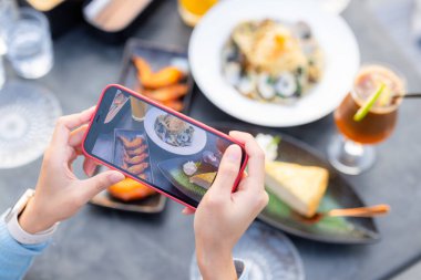 Kadın restoranda fotoğraf çekmek için cep telefonu kullanıyor.