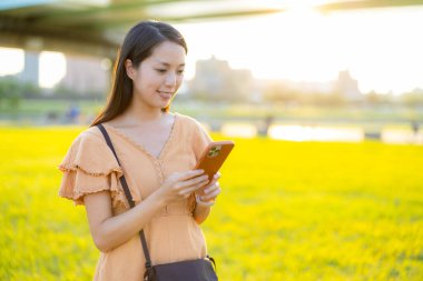 Parkta güneş ışığı altında akıllı telefon kullanan kadın. 