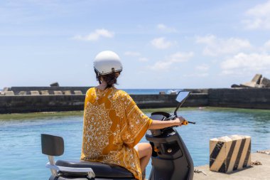 Seyahat eden kadın deniz kenarında motosiklet sürüyor.