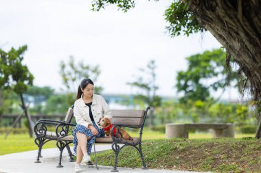 Kadın parka gider ve köpeğiyle bankta oturur.