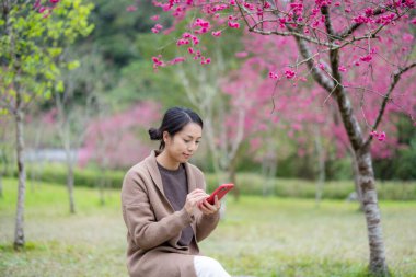 Kadın parkta cep telefonu kullanıyor.