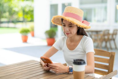 Kadınlar akıllı telefon kullanır ve açık hava kahve dükkanında kahvelerini içerler.