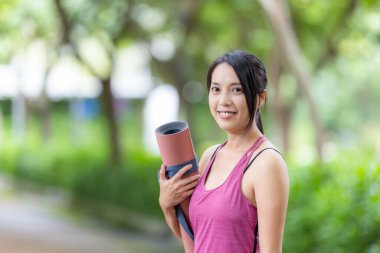 Spor kadını parkta yoga minderiyle bekliyor.