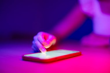 Elini pembe ışıkta cep telefonuna koy.