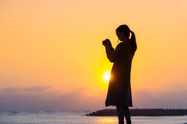 Silhouette of woman use camera to take photo at sunset in the beach