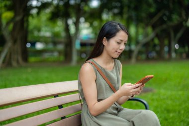 Kadınlar akıllı telefon kullanır ve parkta bankta otururlar.