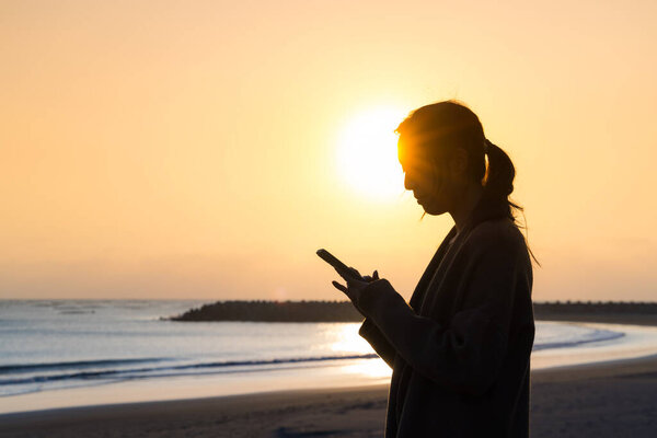Silhouette of Woman use mobile phone at sunset in the beach