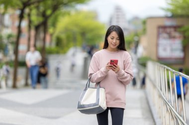 Kadın cadde boyunca yürür ve cep telefonu kullanır