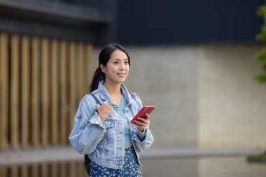 Kadın cep telefonu kullanıyor ve şehirde yürüyor.