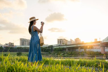 Kadın, Taipei 'nin nehir kenarındaki parkında fotoğraf çekmek için dijital kamera kullanıyor.