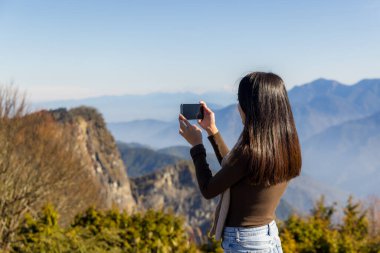 Yürüyüş yapan kadın, dağda fotoğraf çekmek için cep telefonu kullanıyor.