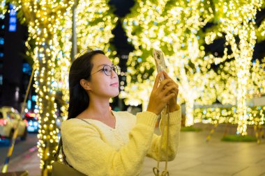 Kadın dışarıda fotoğraf çekmek için cep telefonu kullanıyor.