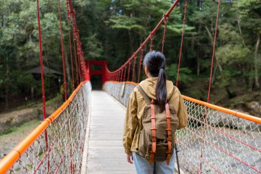Kadın yürüyüşe çıkıp asma köprü boyunca yürür.