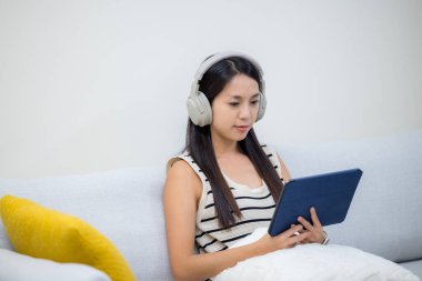 Kadın kulaklık dinler ve evde tablet bilgisayar kullanır.