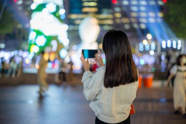 Turist kadın gece şehirde fotoğraf çekmek için cep telefonu kullanıyor.