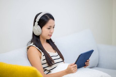 Kadın kulaklık dinler ve evde tablet bilgisayar kullanır.
