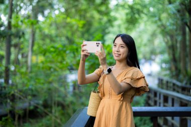 Kadın parkta fotoğraf çekmek için cep telefonu kullanıyor.