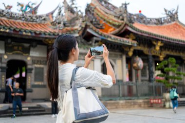 Turist kadın Çin tapınağında fotoğraf çekmek için cep telefonu kullanıyor.