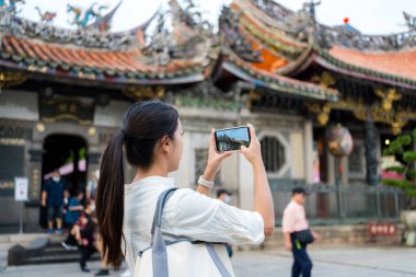 Turist kadın Çin tapınağında fotoğraf çekmek için cep telefonu kullanıyor.