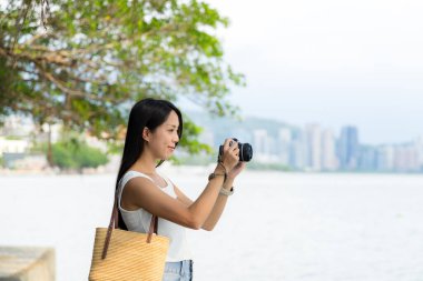 Kadın deniz kenarında fotoğraf çekmek için dijital kamera kullanıyor.