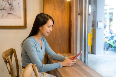 Kadın cep telefonuyla çalışıyor ve kahve dükkanında oturuyor.