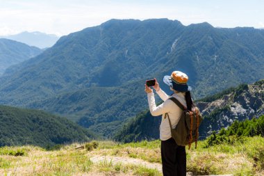Yürüyüş yapan kadın, dağın üzerinden fotoğraf çekmek için dijital kamera kullanıyor.