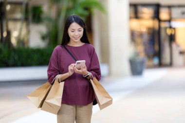 Kadın meydanda alışveriş çantasıyla cep telefonu kullanıyor.