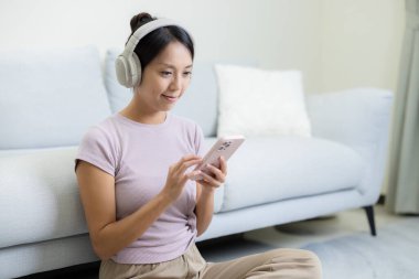 Woman listen to music and use of mobile phone at home clipart