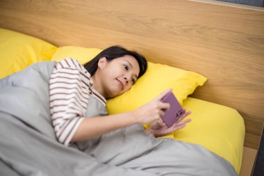 Kadın akıllı telefon kullanır ve yatağa uzanır.