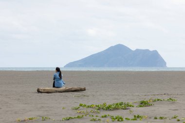 Kadın sahilde oturur ve Yilan 'daki Guishan' a bakar.