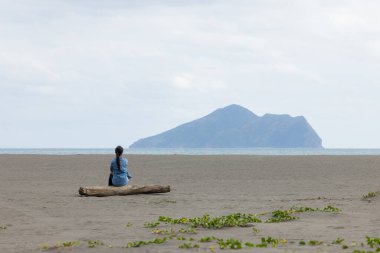 Kadın sahilde oturur ve Yilan 'daki Guishan' a bakar.