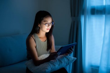 Gözlüklü ve akşamları dijital tablet kullanan bir kadın.
