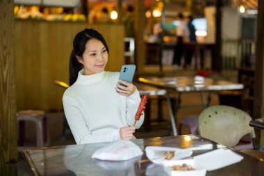 Kadın markette Tayvan sosisiyle fotoğraf çekmek için cep telefonu kullanıyor.