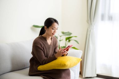 Ev hanımı cep telefonu kullanır ve evdeki kanepeye oturur.