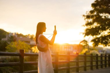 Kırsal kesimde güneş altında cep telefonuyla fotoğraf çeken bir kadın.