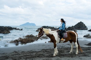Tourist woman ride a horse beside the sea beach clipart