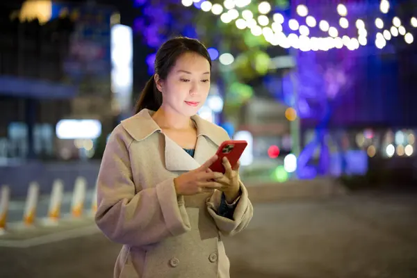 女人在城市中使用移动电话在夜间 免版税图库图片