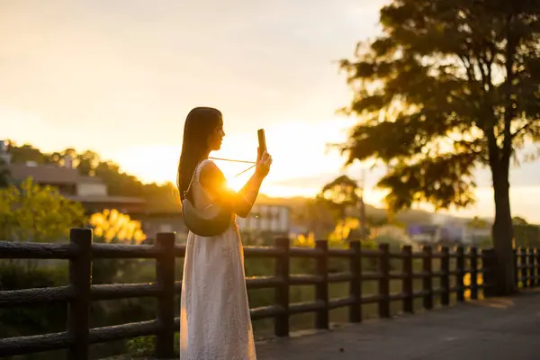女性は田舎の日焼けの下で携帯電話で写真を撮る ロイヤリティフリーのストック写真