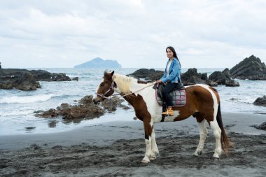Tourist woman ride a horse beside the sea beach clipart