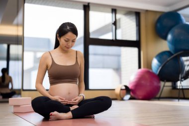 Asyalı hamile kadın spor kıyafetleriyle karnına sarılıyor.