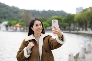 Kadın parkta selfie çekmek için cep telefonu kullanıyor.
