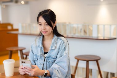 Kadın kahve dükkanında cep telefonunu kontrol ediyor.