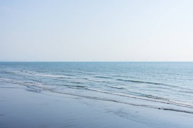 Okyanusun üzerinde rüzgar türbini olan bir sahil.