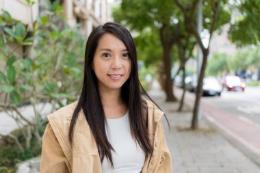 Asyalı kadın dışarıda kameraya gülümsüyor.