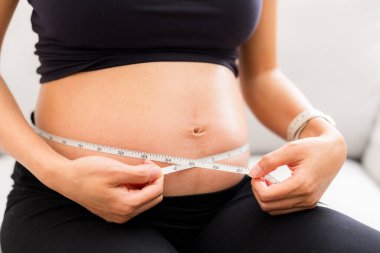 Kanepede oturan hamile kadın göbeğini ölçer.