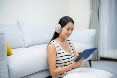 Kadın evde müzik dinliyor ve tablet bilgisayardan izliyor.