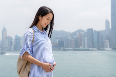 Hamile kadın, Hong Kong şehrinin arka planında karnını tutuyor.